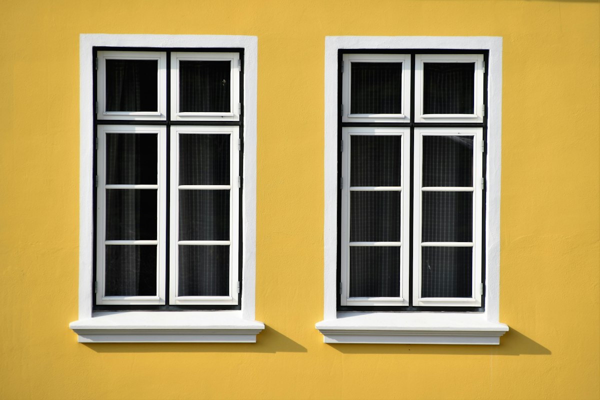 Deux fenêtres à petits-bois et encadrement blanc sur une façade jaune